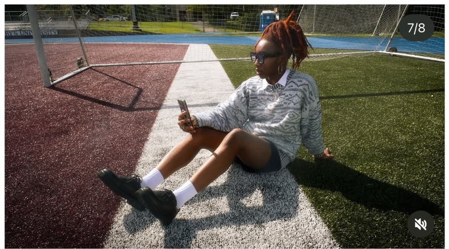 Stellae rests on the turf inside a soccer goal, phone in hand